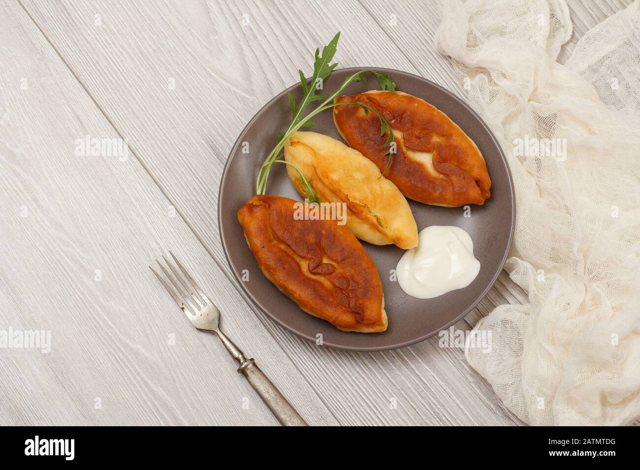 Plaque avec tartes fries, crème aigre et fourchette, gaze blanche sur planches en bois. Vue de dessus. Banque D'Images