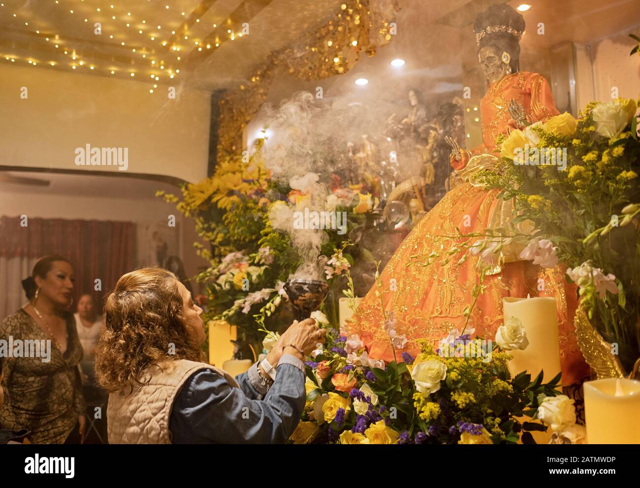 Un adorateur mexicain américain souffle de la fumée à une statue de Santa Muerte dans un temple à la maison à Queens, New York City. Banque D'Images