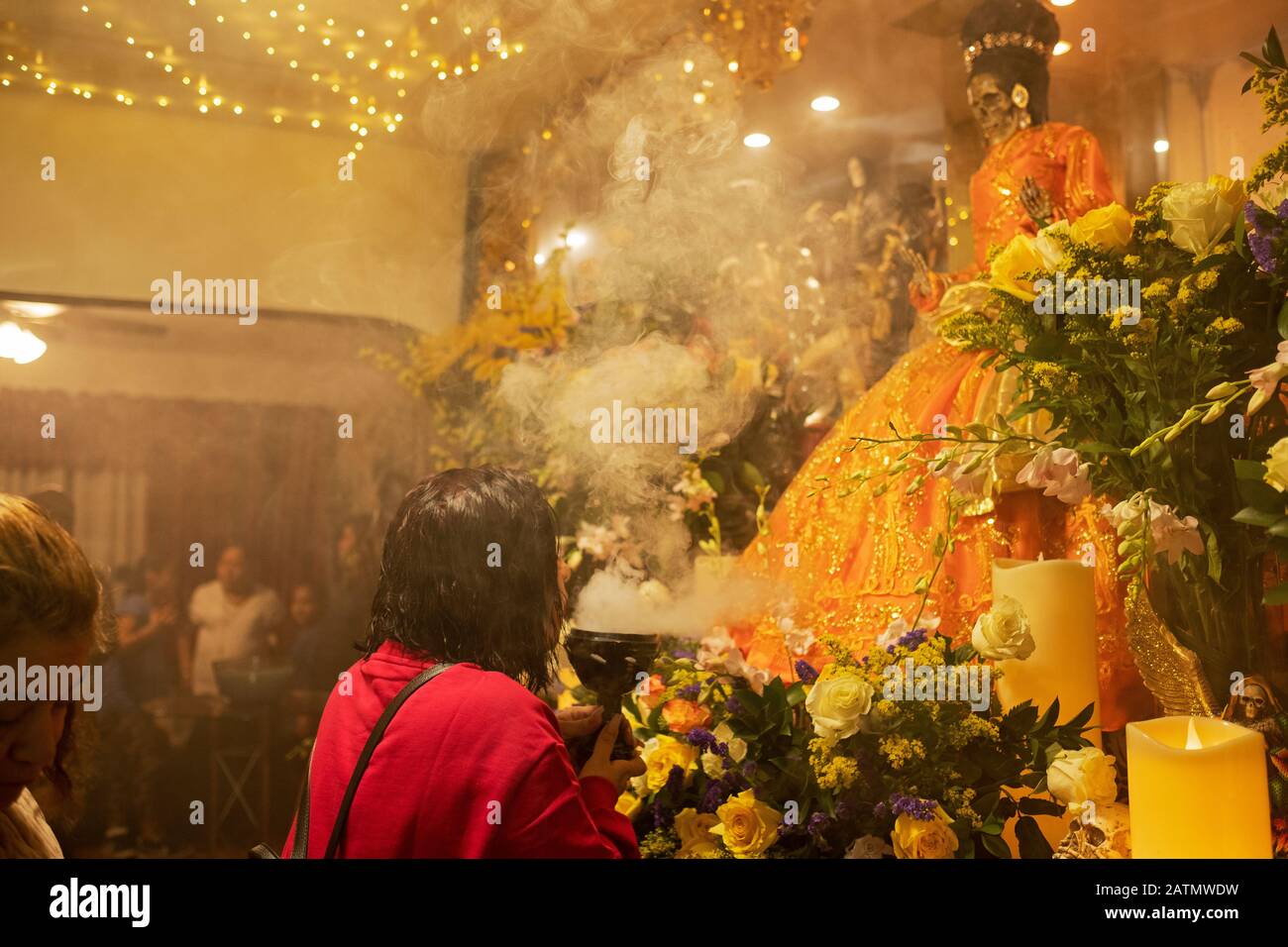 Un adorateur mexicain américain souffle de la fumée à une statue de Santa Muerte dans un temple à la maison à Queens, New York City. Banque D'Images