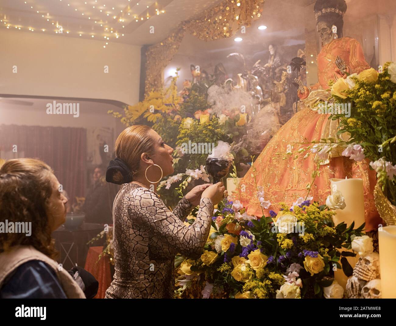 Une trans prêtresse souffle de la fumée à une statue de Santa Muerte dans un temple maison à Queens, New York City. Banque D'Images