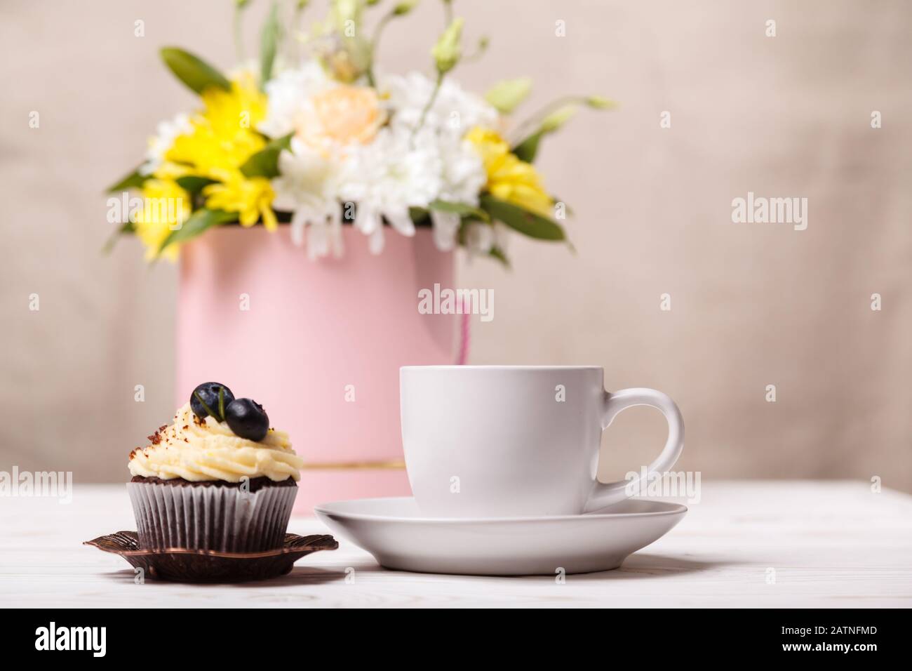 Une tasse de café blanc et un cupcake avec crème fouettée et bleuets, un bouquet de fleurs printanières à l'arrière-plan. Romantique amour arrière-plan. Valen Banque D'Images