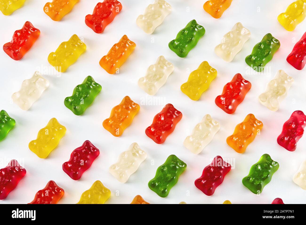 Vue sur la couche plate des bonbons colorés à l'ours en forme de gummy, conçus dans une rangée sur fond blanc. Macro de gros plan. Banque D'Images