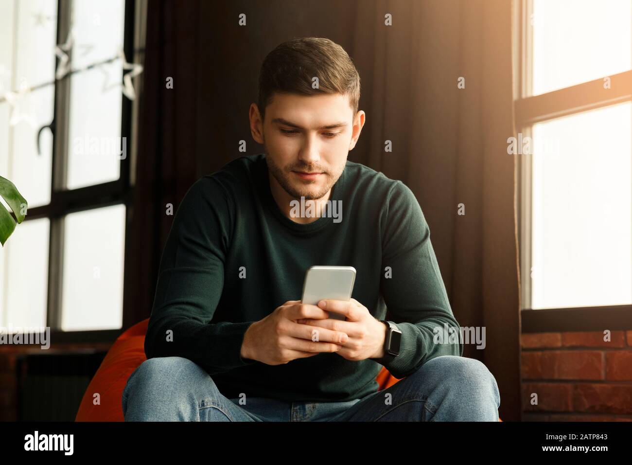 Guy Millénaire Utilisant Smartphone Texting Assis Dans Beanbag Chaise Intérieure Banque D'Images