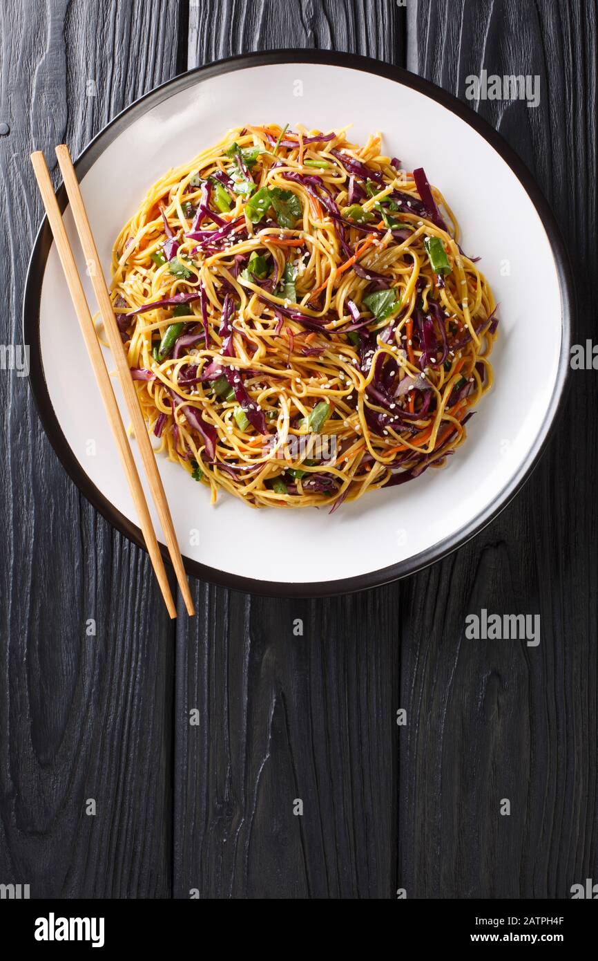 Salade de nouilles asiatiques avec chou rouge émincé, carottes julientées dans une vinaigrette épicée aux arachides dans une assiette sur la table. Vue de dessus verticale de Banque D'Images