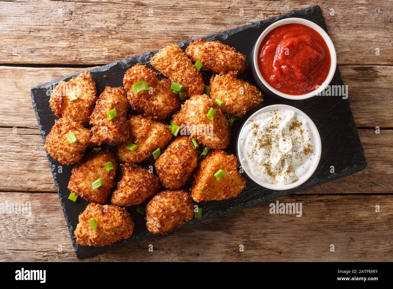 De délicieux pépites de poulet panés avec de la noix de coco servies avec du ketchup et de la mayonnaise près d'une planche en ardoise sur la table. Vue de dessus horizontale de l'abo Banque D'Images