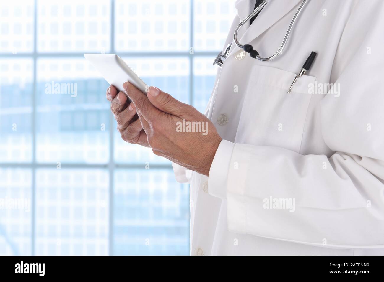Gros plan d'un médecin avec une tablette informatique devant une grande fenêtre dans un établissement médical moderne. L'homme n'est pas reconnaissable. Banque D'Images