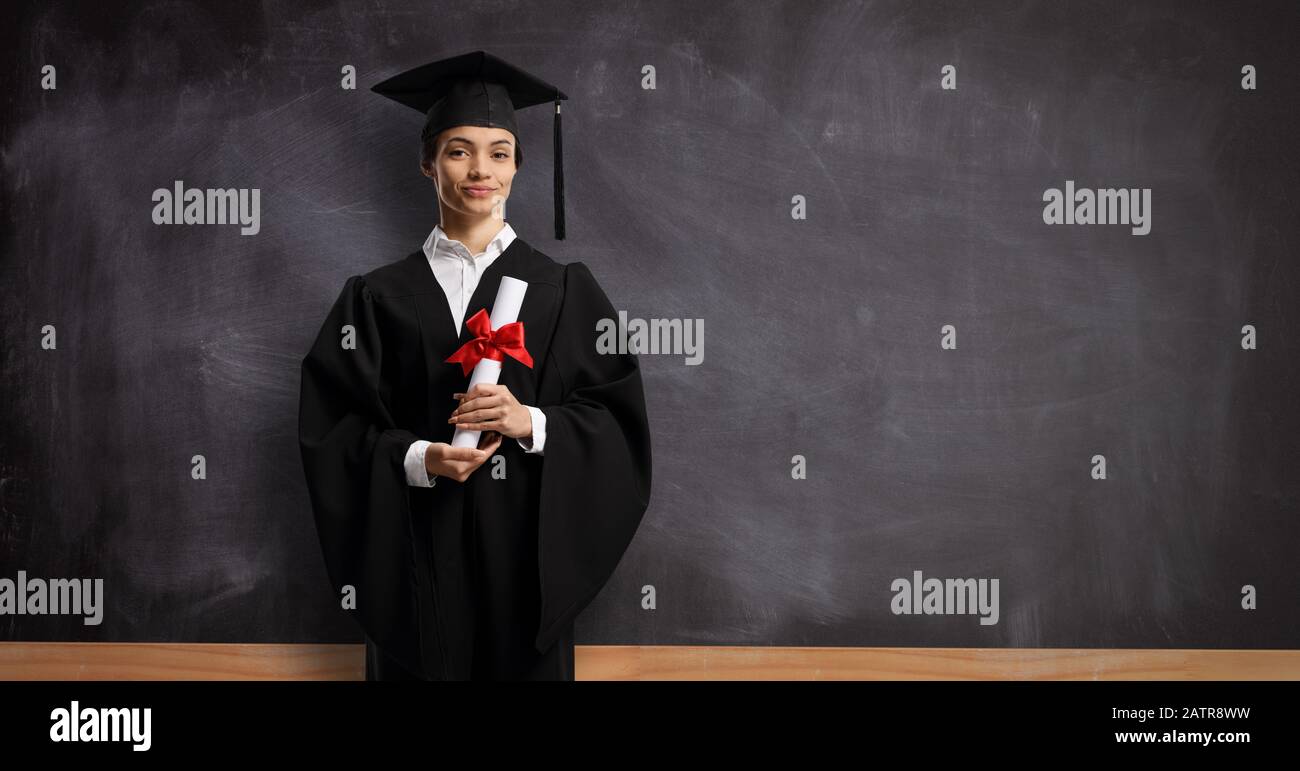 Une étudiante féminine dans une robe de graduation avec un diplôme devant un tableau noir de l'école Banque D'Images