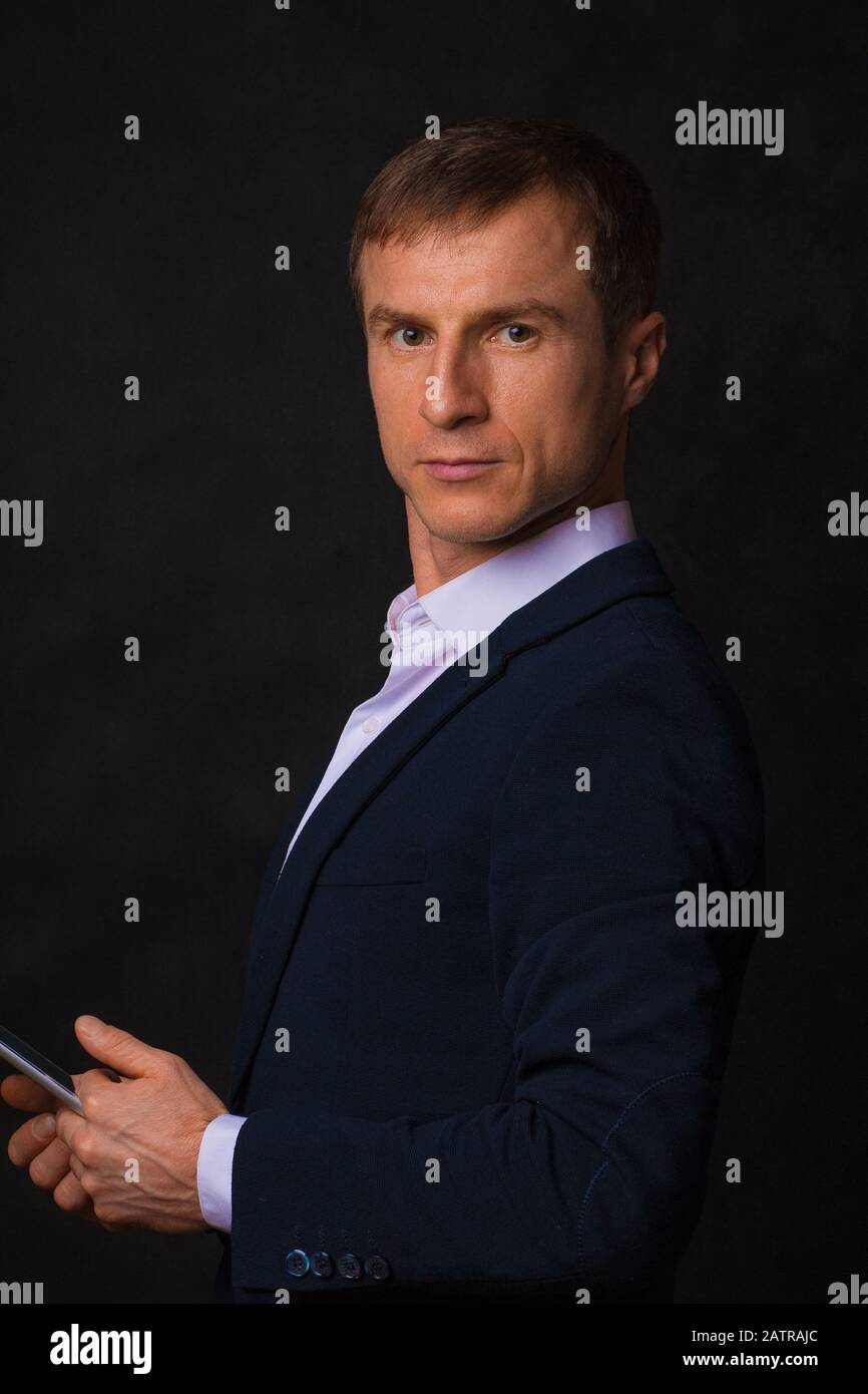 Homme européen dans un costume bleu d'affaires sur un fond noir avec un téléphone dans ses mains. Portrait d'un homme d'affaires. La vie est des personnes réelles, le style de vie, avec Banque D'Images