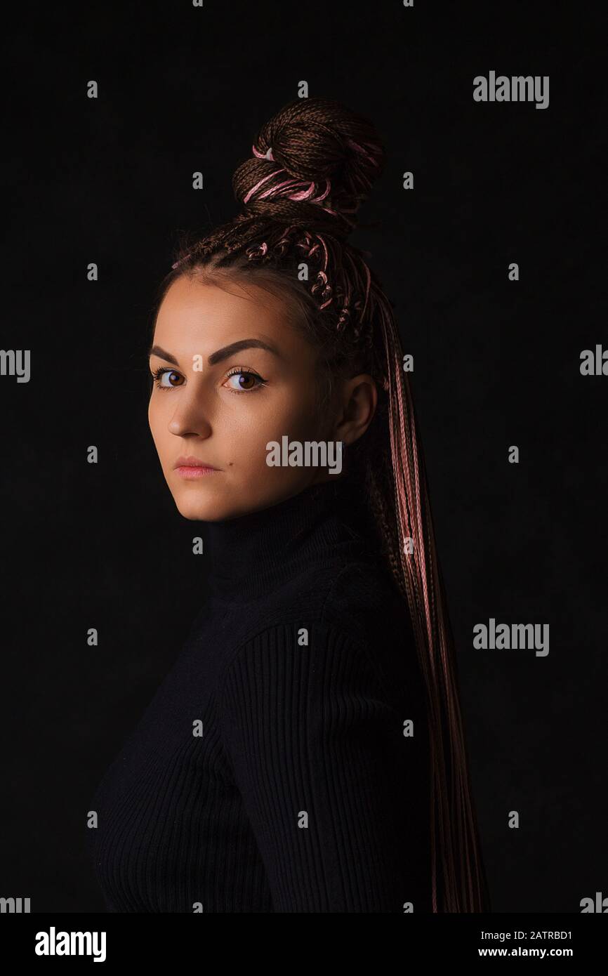 Une belle fille avec des queues de porc afro ou zizi roses et des yeux bruns semble sternly à l'appareil photo sur un fond noir. Portrait avec un ha haut à la mode Banque D'Images