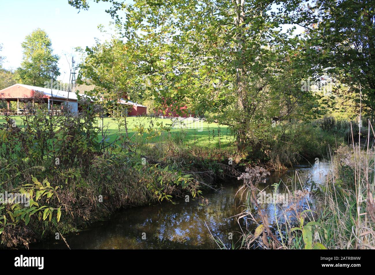 une rivière à côté d'une ferme de campagne avec une grange rouge Banque D'Images