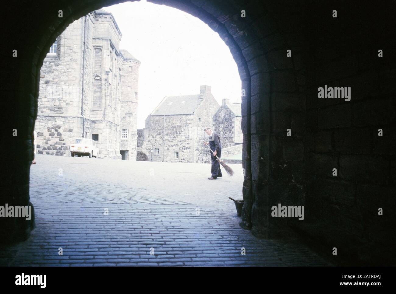 Photo vernaculaire prise sur un film analogique de 35 mm transparent, qui est censé représenter l'homme dans une veste noire marchant sur le trottoir pendant la journée, vu par une arche en silhouette, 1970. Les principaux sujets/objets détectés sont l'hiver, la lumière, la neige et l'ombre. () Banque D'Images