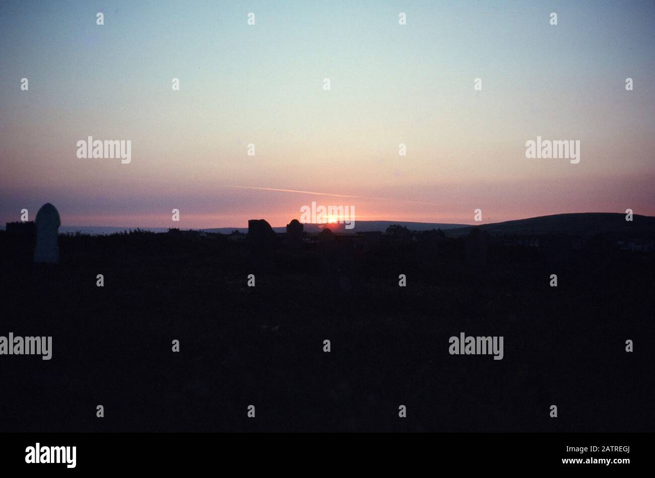 Photographie vernaculaire prise sur une transparence de film analogique de 35 mm, considérée comme une silhouette de maisons au coucher du soleil, 1970. Les principaux sujets/objets détectés sont Sky, Sunset, Dawn, Dusk, Evening, Hill et Sun. () Banque D'Images