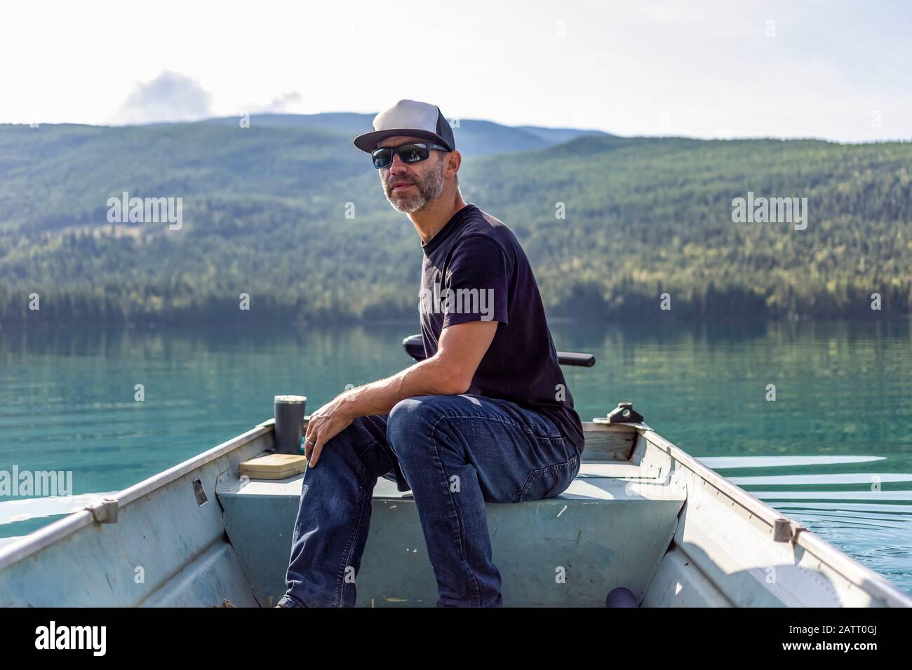 L'homme est assis dans un petit bateau à rames avec moteur sur le lac White, avec l'eau tranquille reflétant la forêt en arrière-plan; Colombie-Britannique, Canada Banque D'Images