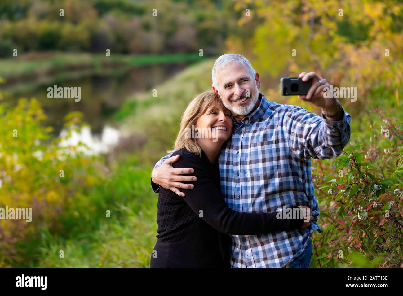 Un couple mature qui profite du temps ensemble et prend un autoportrait tout en admirant le coucher de soleil le long d'une rivière dans une ville garez-vous une chaude soirée d'automne Banque D'Images