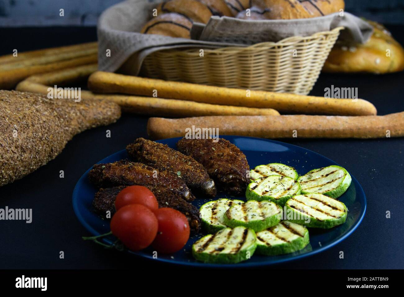 Ailes de poulet frit dans la pâte, avec courgettes grillées et tomates sur la plaque bleue. Banque D'Images