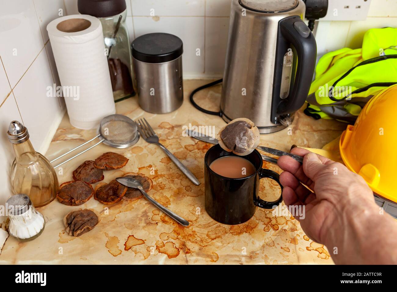 Constructeur faisant une tasse de thé dans sa kitchenette sale à côté de son chapeau de dur et de haut gilet de visibilité Banque D'Images