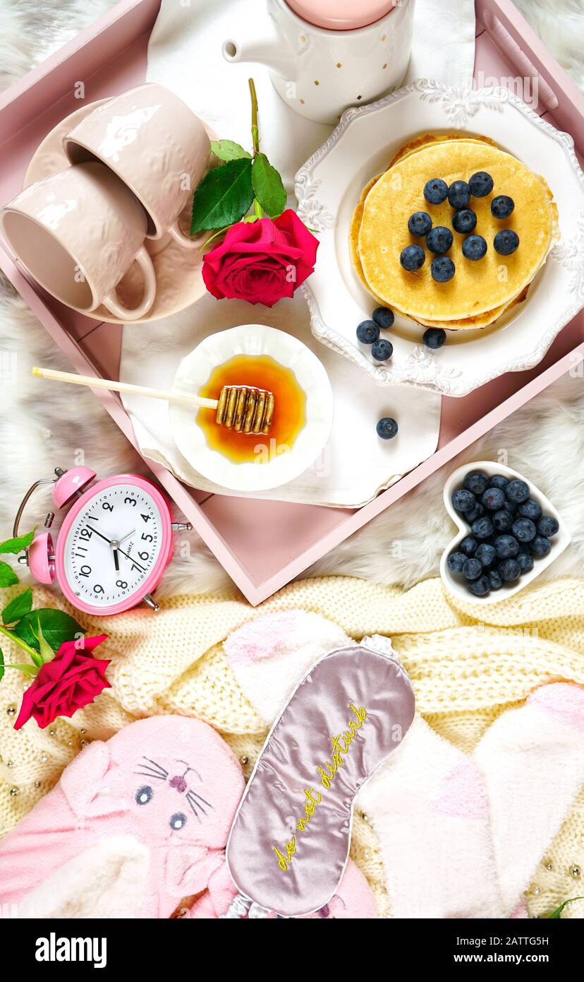 Plateau de petit-déjeuner pancake au lit avec sirop et bleuets fruits mise en page créative plat, vue sur le dessus, avec pantoufles, masque de couchage et chaussettes de lit confortables. Banque D'Images