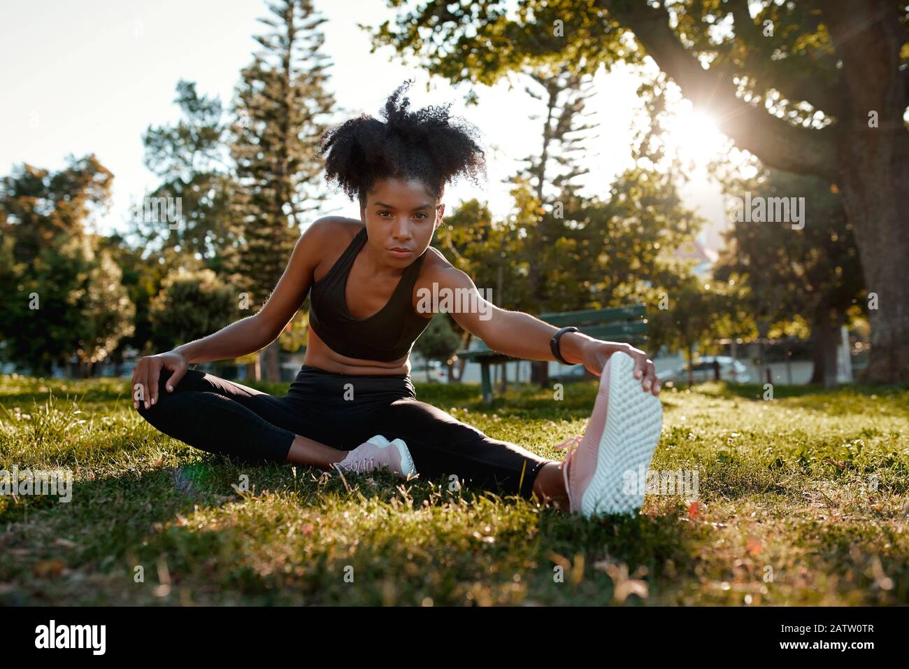 Portrait d'une jeune femme afro-américaine déterminée assise sur l'herbe verte faisant de l'exercice dans le parc - jeune femme noire la réchauffe Banque D'Images