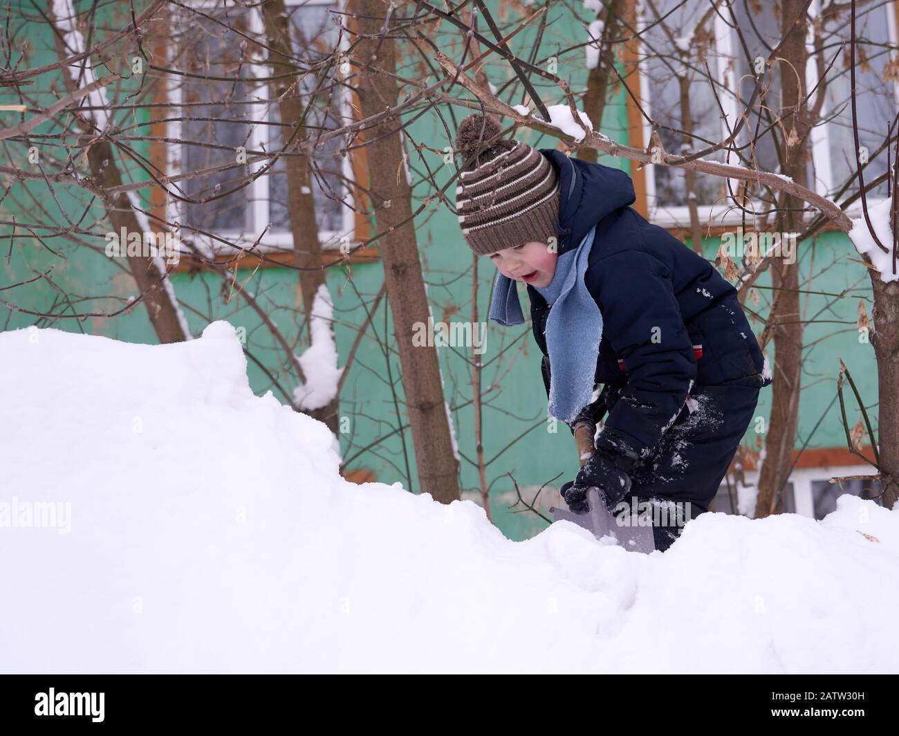 Un garçon dans un chapeau tricoté et avec un foulard en hiver joue dans la neige. Banque D'Images