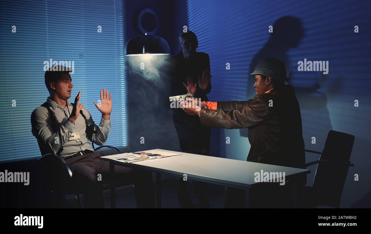 Le délinquant multiracial saisit l'arme et menace de nuire aux détectives pendant le processus d'interrogatoire. Ils ont très peur et se lèvent les mains. Banque D'Images