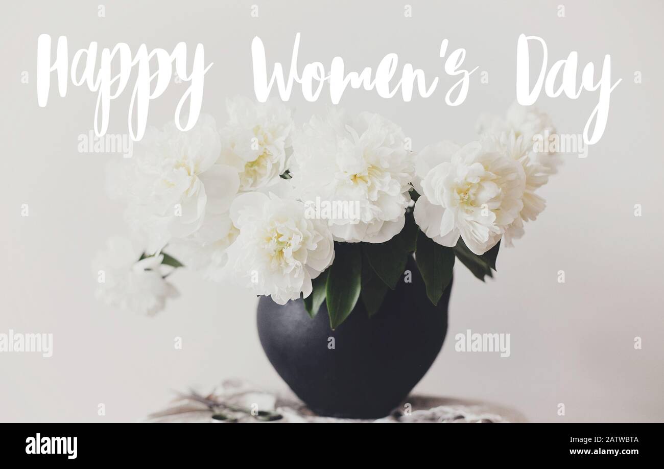 Happy Women's day text manuscrit sur un bouquet de pivoine élégant dans un vase en argile noire sur tissu lin avec ciseaux sur fond rustique. Pivoines blanches rurales Banque D'Images