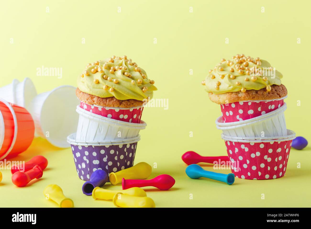 Des cupcakes rigoles dans des tasses à pois drôles et des ballons dégonflés sur fond jaune, gros plan, espace de copie Banque D'Images