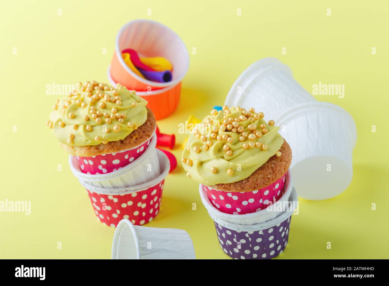 Des cupcakes rigoles dans des tasses à pois drôles et des ballons dégonflés sur fond jaune, gros plan, espace de copie Banque D'Images