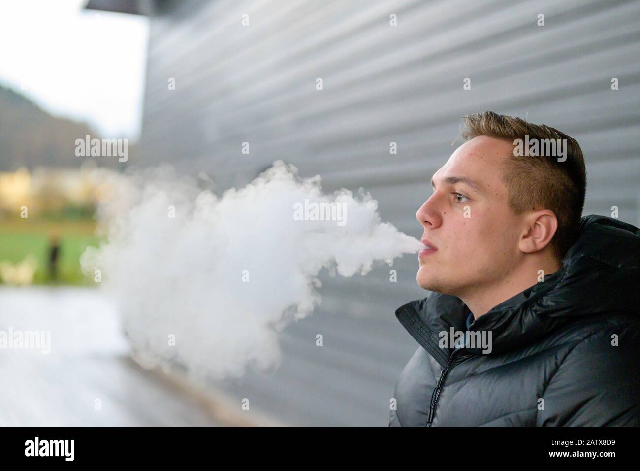 Un jeune homme qui fume une cigarette lectronique en plein air en hiver  exhalant une bouffe de fume dans un concept de sant et de toxicomanie  avec espace de copie Photo Stock -
