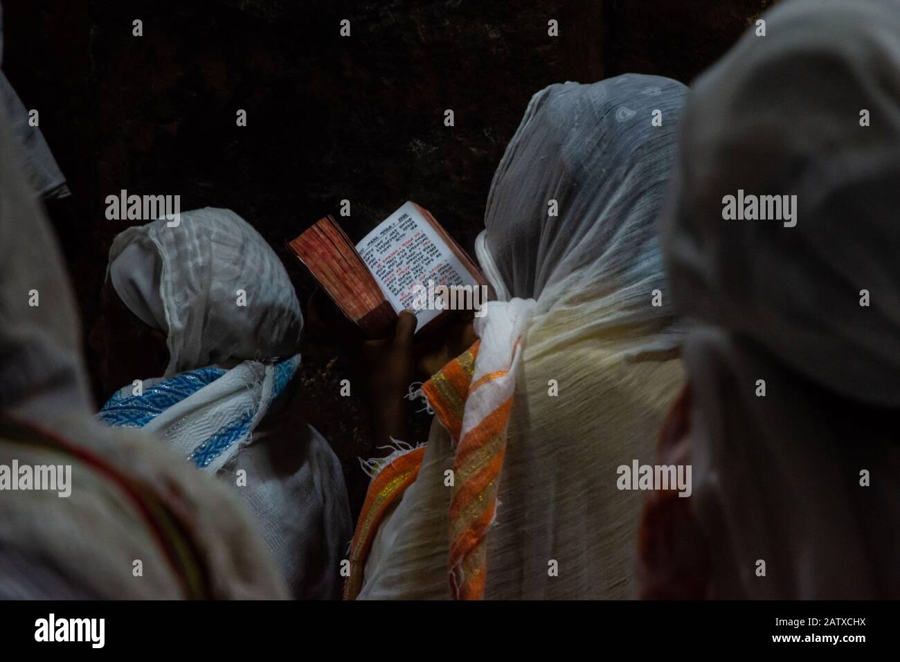 Lalibela, Ethiopie - Nov 2018: Les femmes vêtues de blanc traditionnel, assis au crépuscule et lire livre de prières à côté des églises souterraines de la Banque D'Images