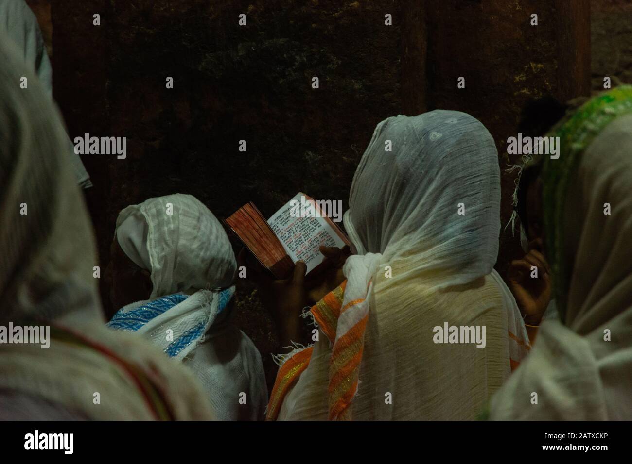 Lalibela, Ethiopie - Nov 2018: Les femmes vêtues de blanc traditionnel, assis au crépuscule et lire livre de prières à côté des églises souterraines de la Banque D'Images