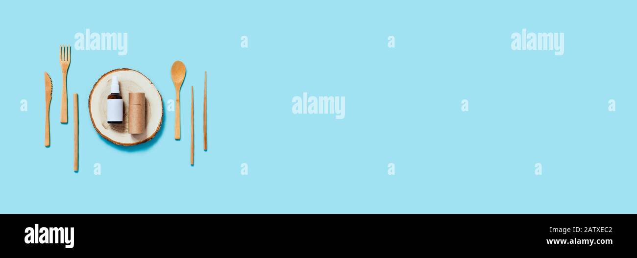 Bannière Web zéro déchet. Vaisselle en bambou naturel, tube d'artisanat, plateau en bois, huile naturelle dans le spray sur fond bleu. Couche plate, vue supérieure, espace de copie. Banque D'Images