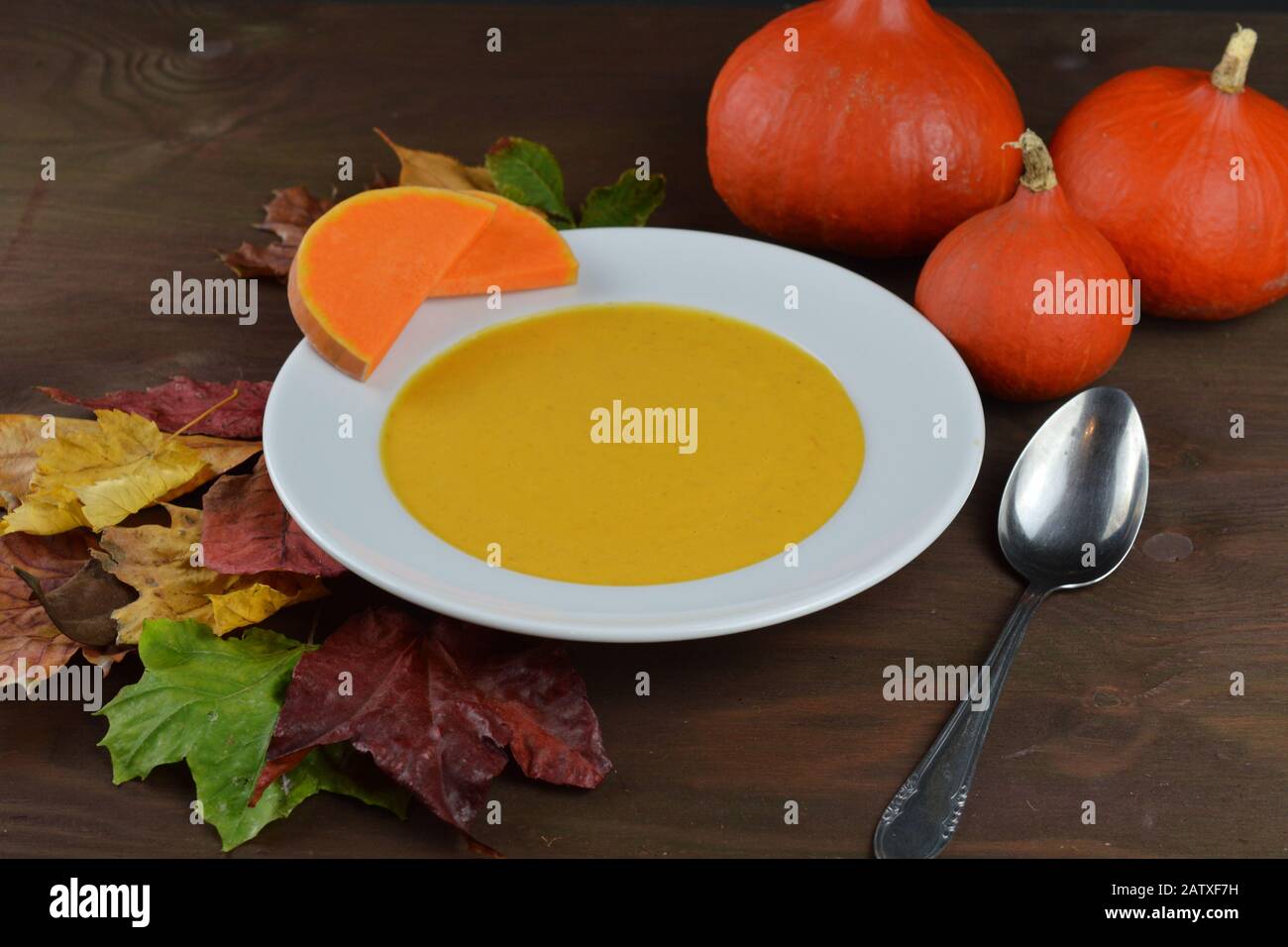 soupe de citrouille d'automne dans un bol avec citrouilles hokkaido, feuilles et cuillère sur une table en bois brun Banque D'Images