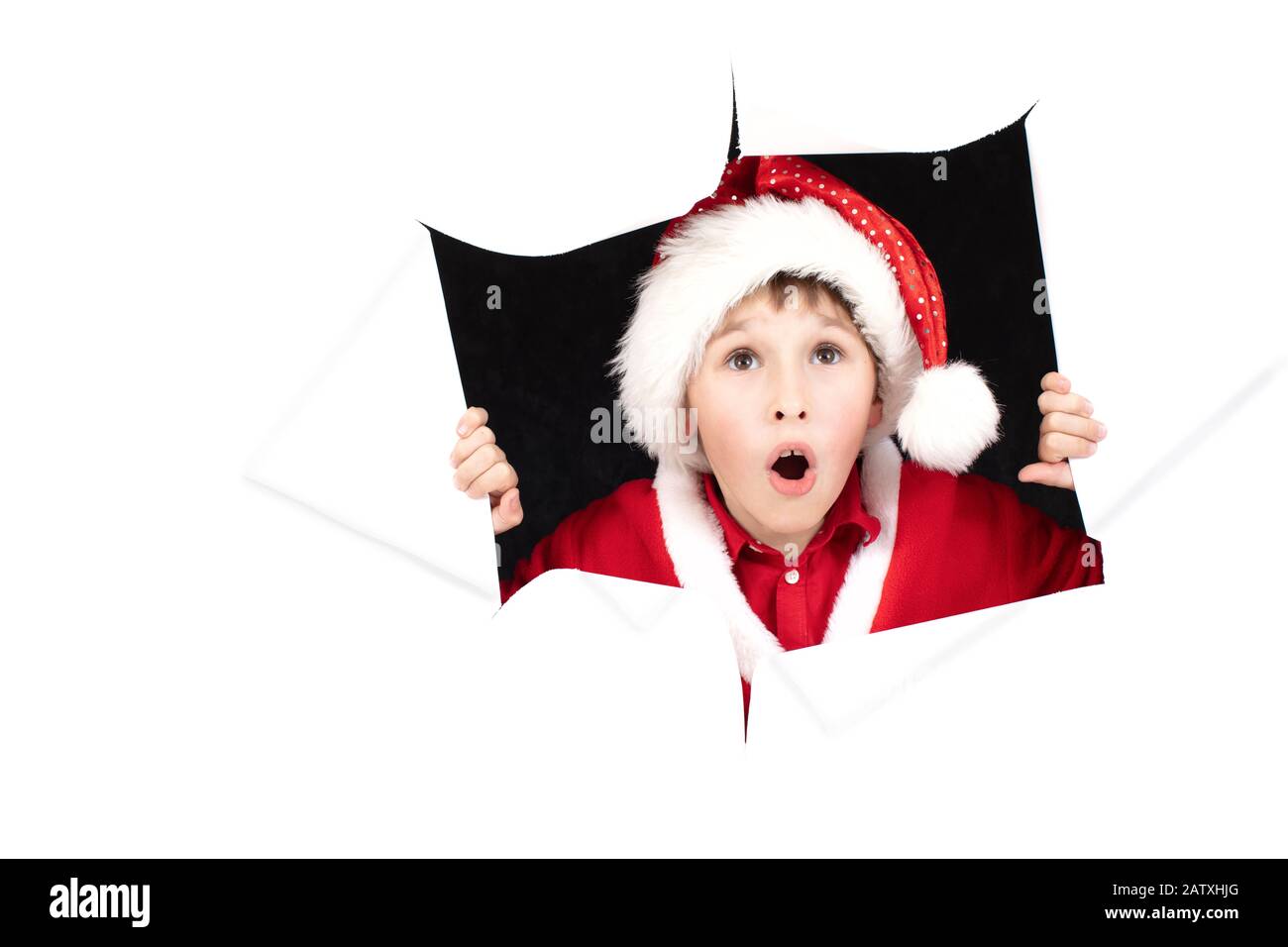 Enfant le Père Noël a l'air d'un trou dans le papier. Le garçon de Noël est surpris. Surprise du nouvel an. Concept de vacances de Noël Banque D'Images