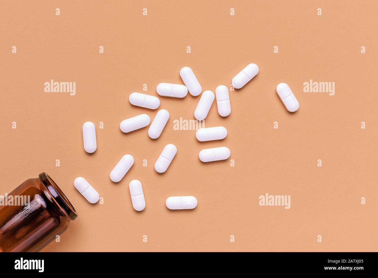 Pilules ovales blanches recouvertes de film déversées de la bouteille sur fond pastel avec espace de copie, vue de dessus Banque D'Images