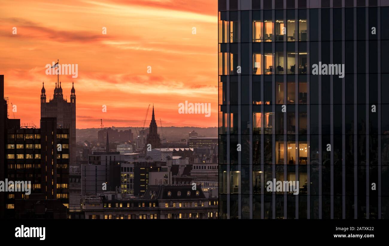 Coucher De Soleil À Londres. Vue sur la capitale britannique avec le drapeau surmonté de Victoria Tower, le Palais de Westminster, contrastant avec les gratte-ciel. Banque D'Images