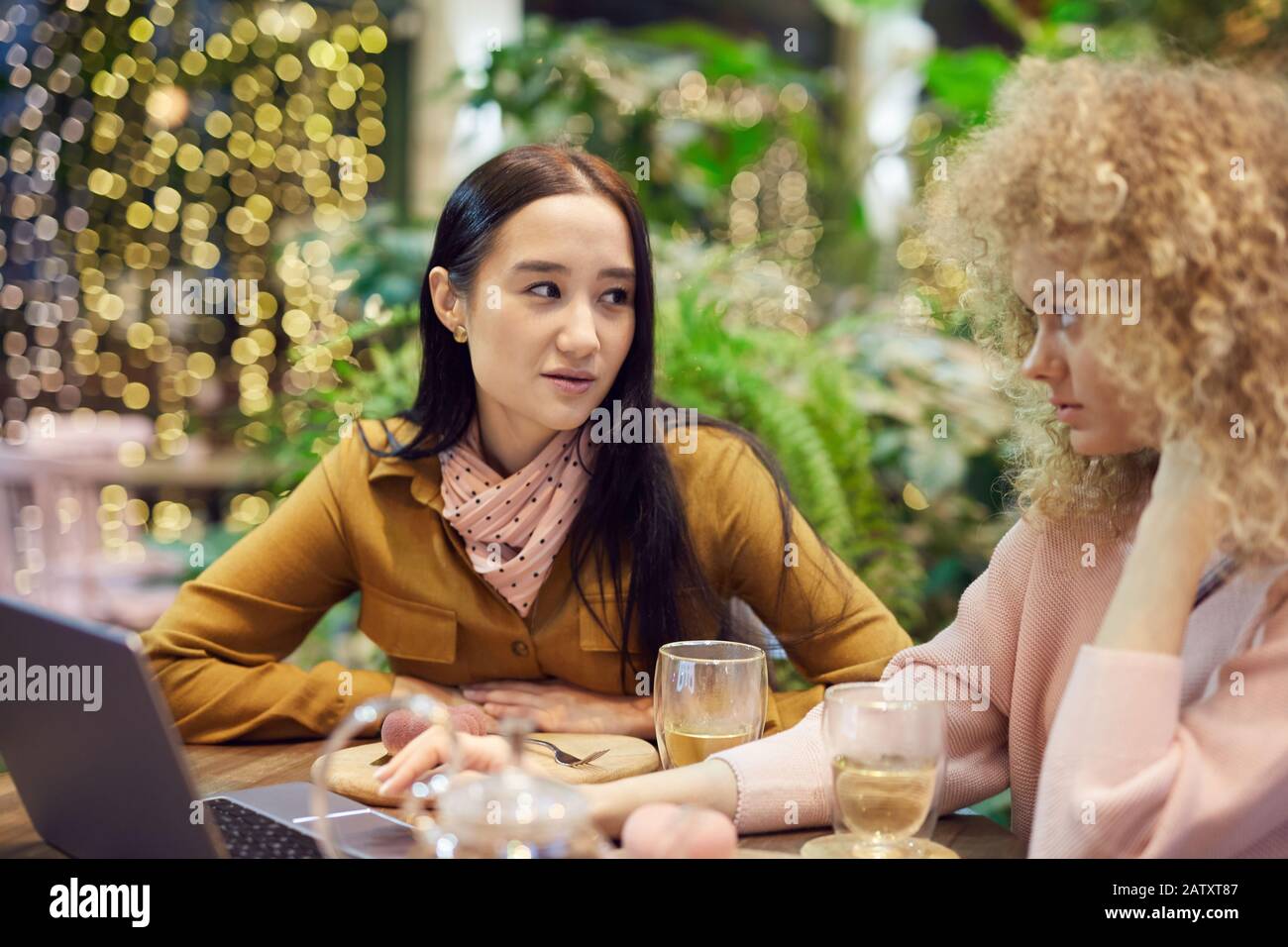 Jeune femme asiatique discutant d'un projet avec sa collègue lorsqu'ils sont assis à la table avec un ordinateur portable dans un café Banque D'Images