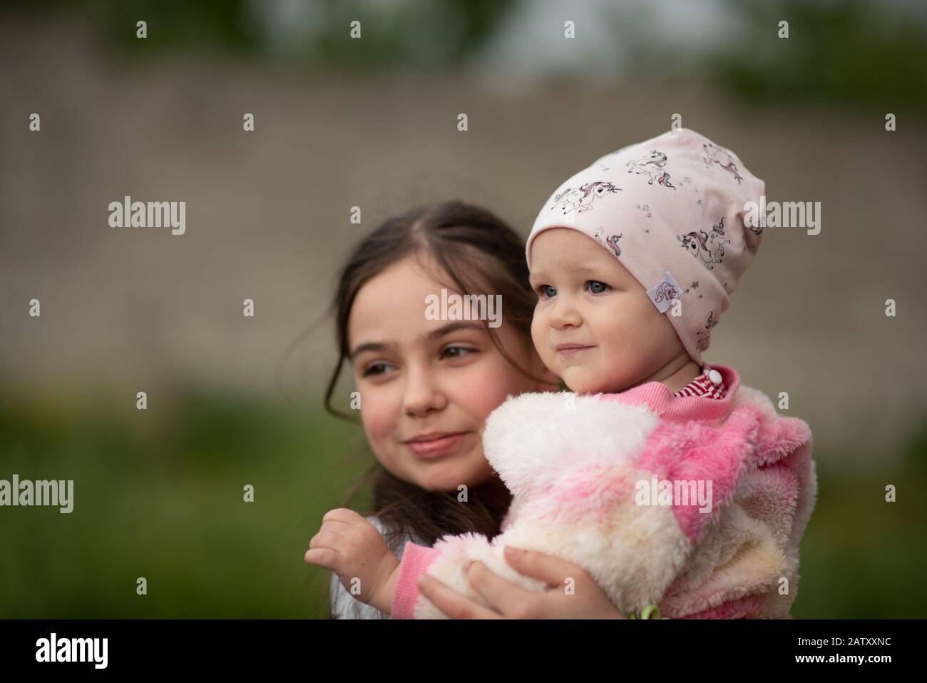 jolie jeune fille souriante et souriante debout sur une pelouse portant sa petite sœur dans ses bras. elle tient sa sœur dans ses bras. Fille de 10 ou 11 ans et 1 an Banque D'Images