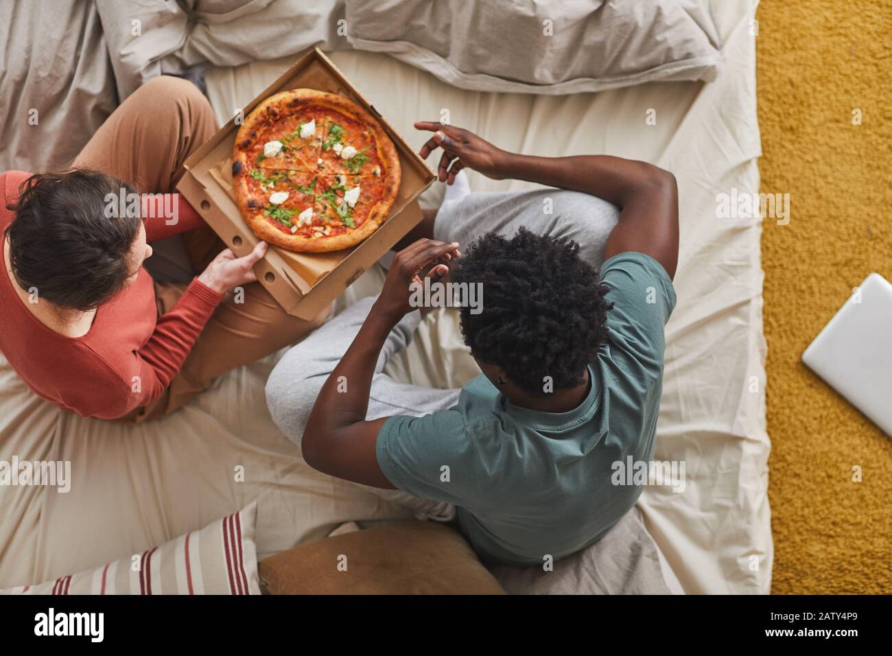 Vue sur le grand angle des jeunes couples assis sur le lit et manger de la pizza ensemble dans la chambre Banque D'Images