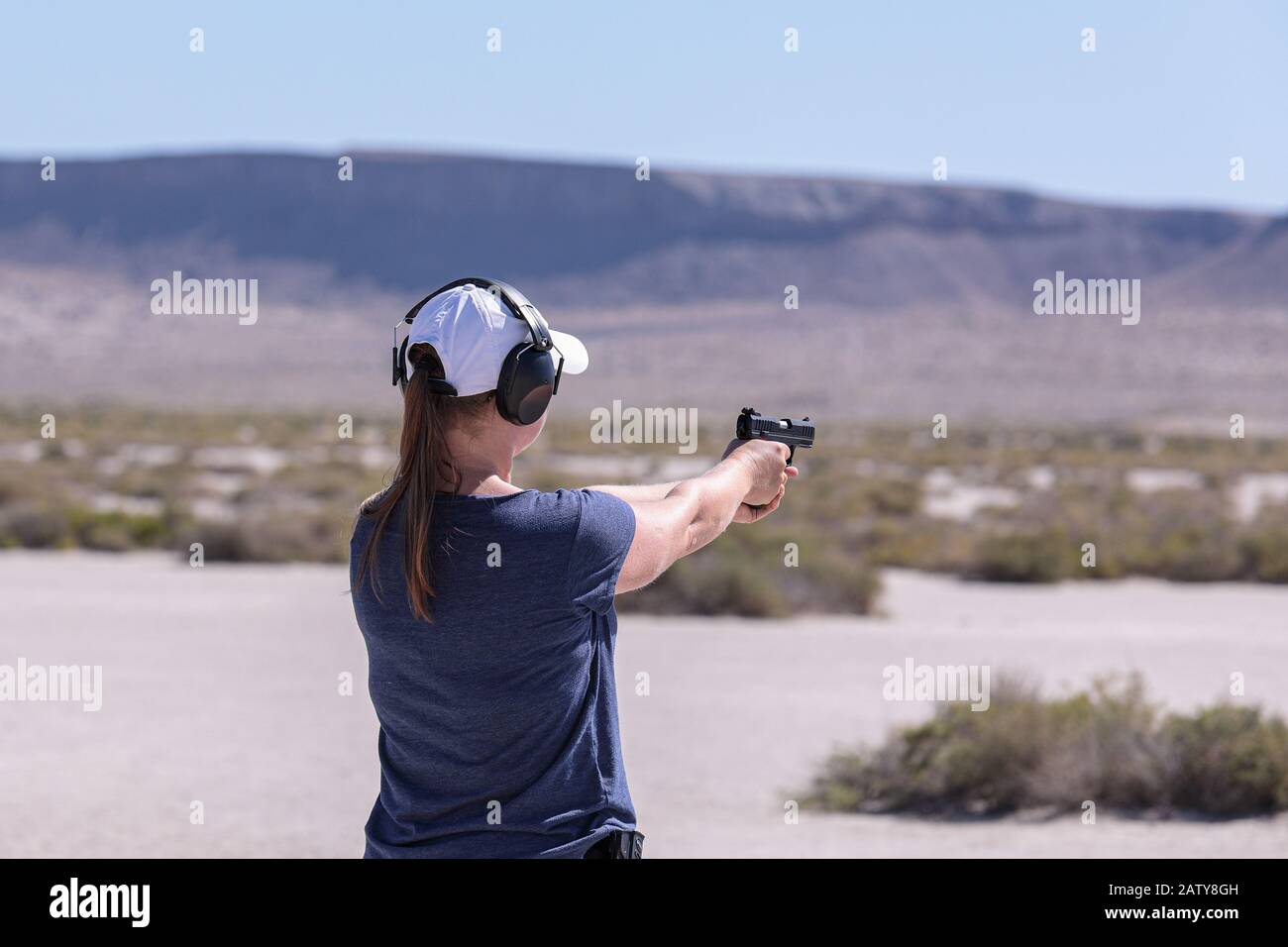 Femme en t-shirt bleu et casquette de baseball blanche pratiquant le tir ciblé à partir d'un pistolet 22 LR. Banque D'Images