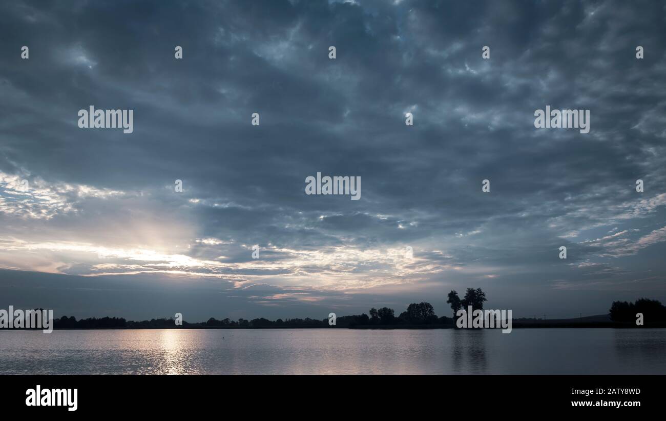 Le soleil brille à travers les nuages bleus au-dessus de l'eau, vue du soir Banque D'Images