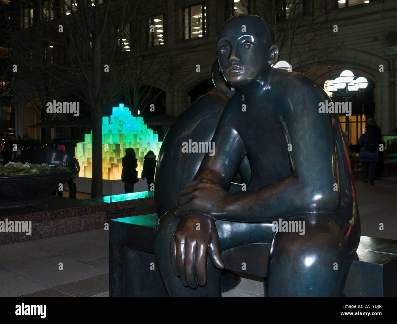 Deux hommes sur un banc et la Pyramide à Canary Wharf pendant Winter Lights 2020 dans le noir de nuit Banque D'Images