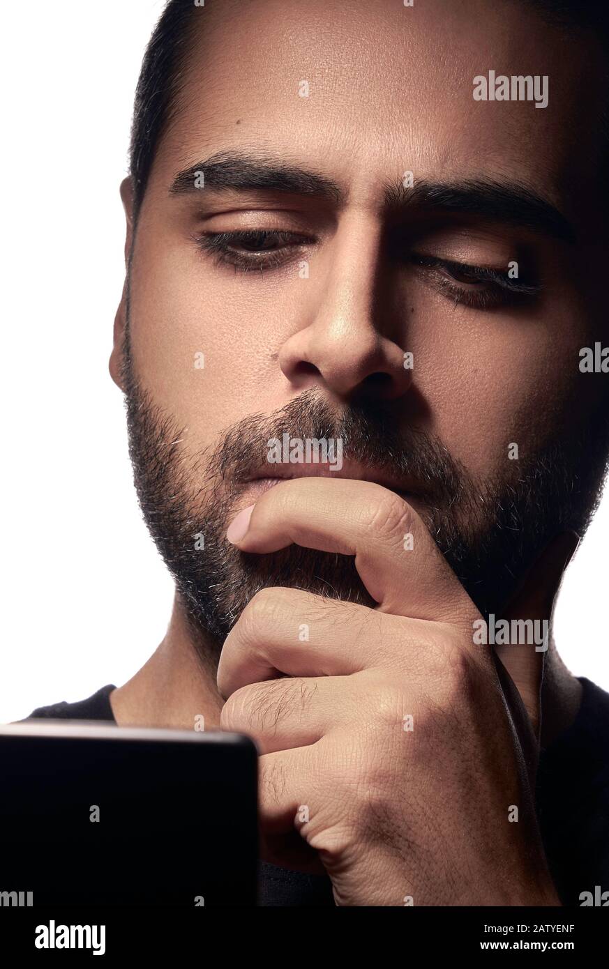 Un gars arabe barbu à l'aide d'un smartphone et pensant avec sa main sur la bouche Banque D'Images