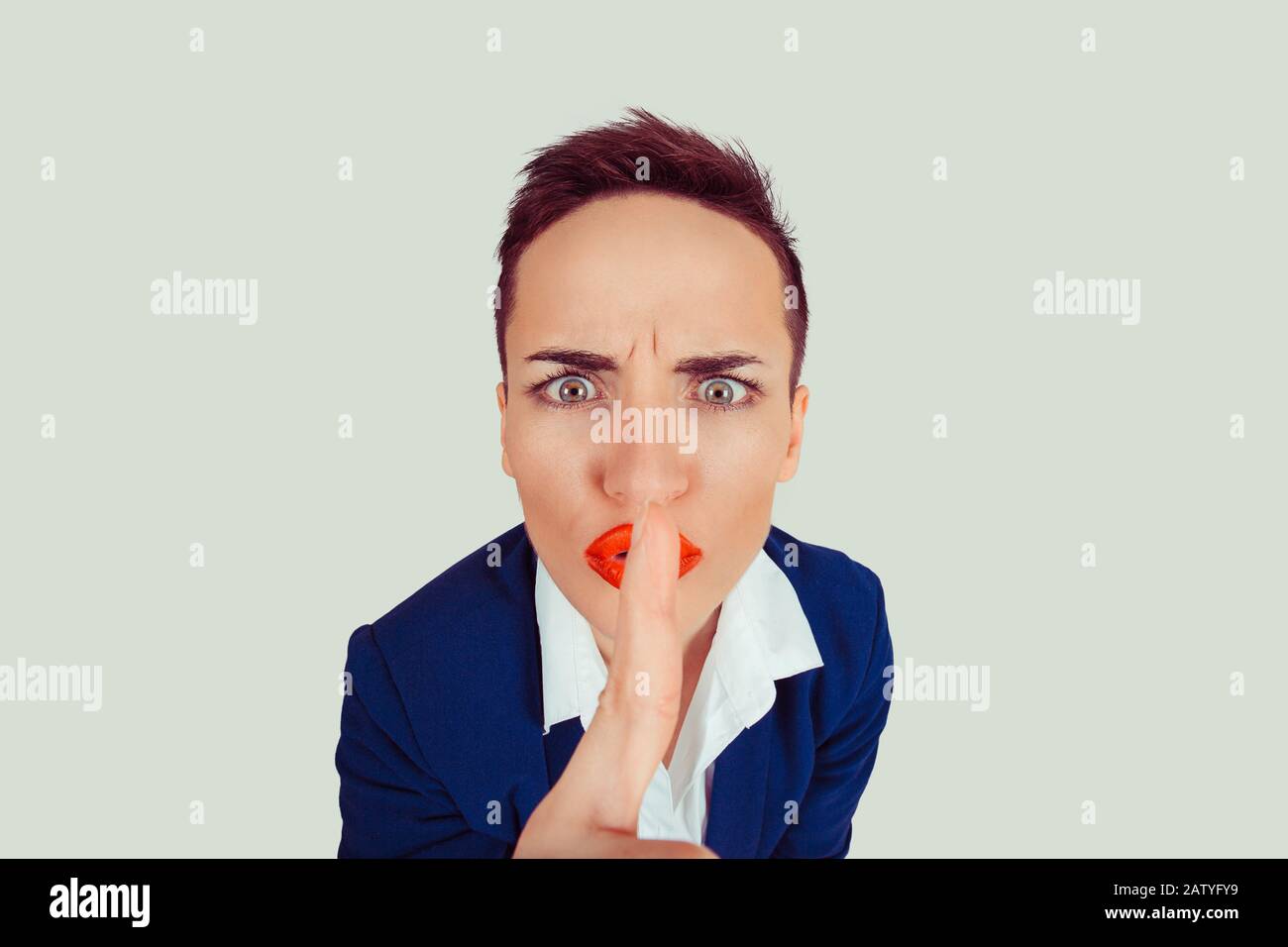 Une femme en colère a eu un grand œil pour demander le silence ou le secret avec le doigt sur les lèvres, rougir le geste de la main fond vert clair. Jolie fille plaçant les doigts sur les lèvres Banque D'Images