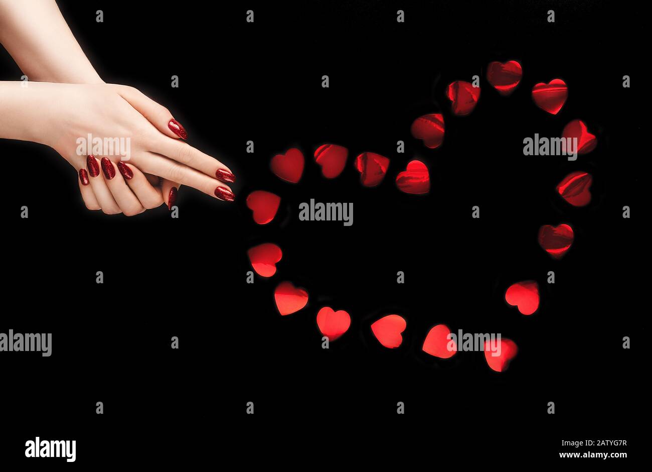 Belles mains féminines avec des confettis rouges vibrants disposés dans une forme de coeur sur fond noir isolé. Toile de fond pour votre conception. Créatif branché f Banque D'Images