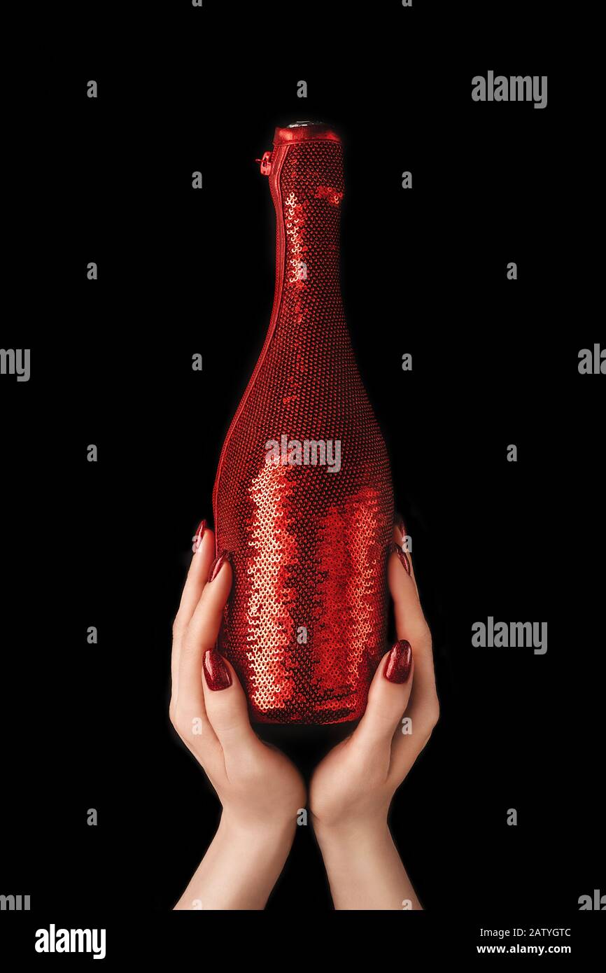 De belles mains féminines avec une manucure rouge à la mode tenant une bouteille de champagne dans une housse couchée avec des séquelles rouges éclatantes sur fond noir isolé. Moc Banque D'Images