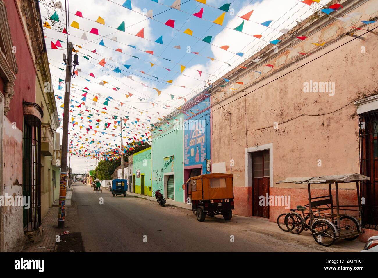 Pédicab (vélo taxi) dans une rue coloniale à Hunucma, Yucatan, Mexique. Les drapeaux de Papel Picado volent en hauteur. Banque D'Images