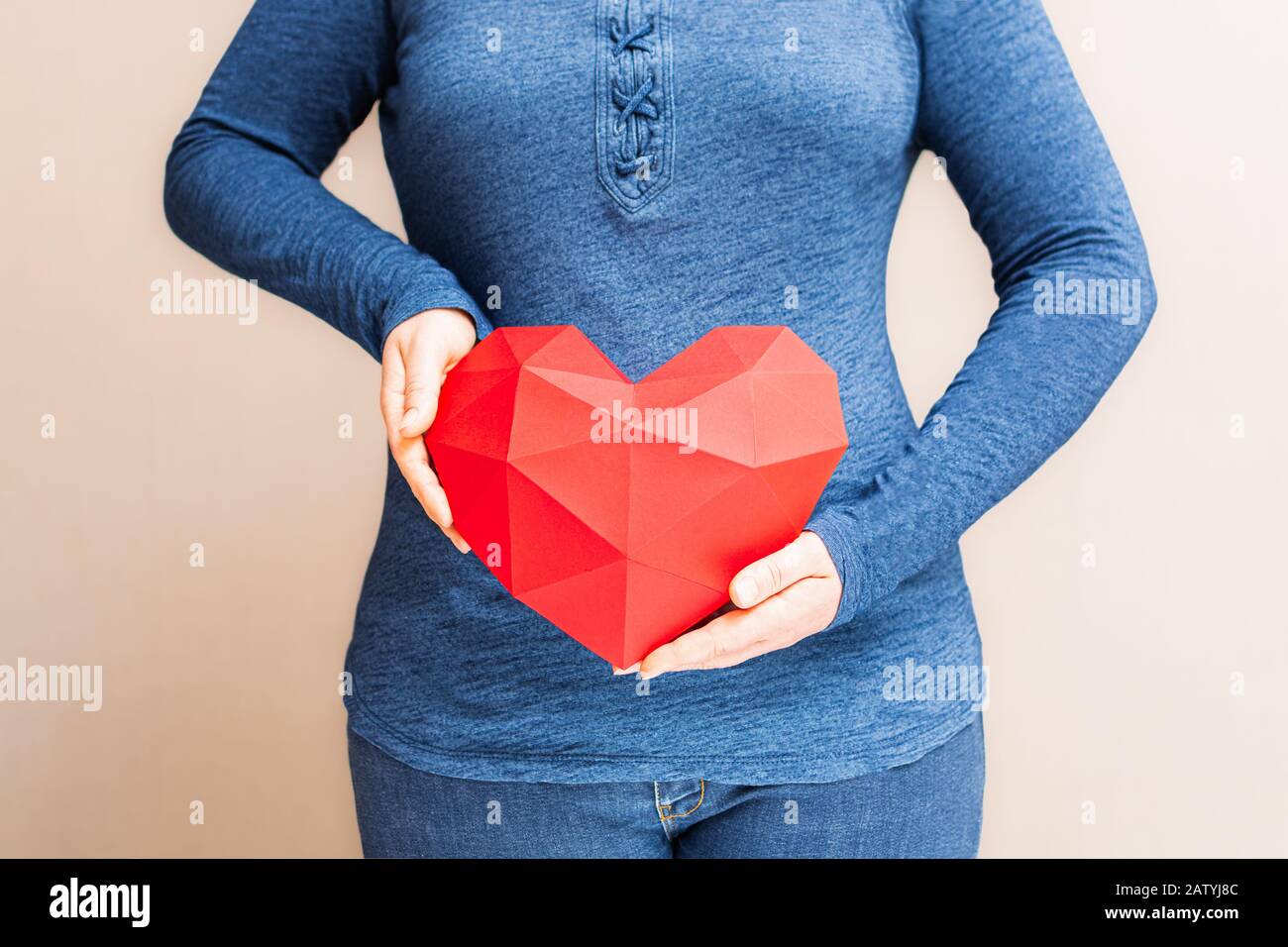 Jeune femme tenant le coeur rouge polygonal en forme de losange devant son corps Banque D'Images