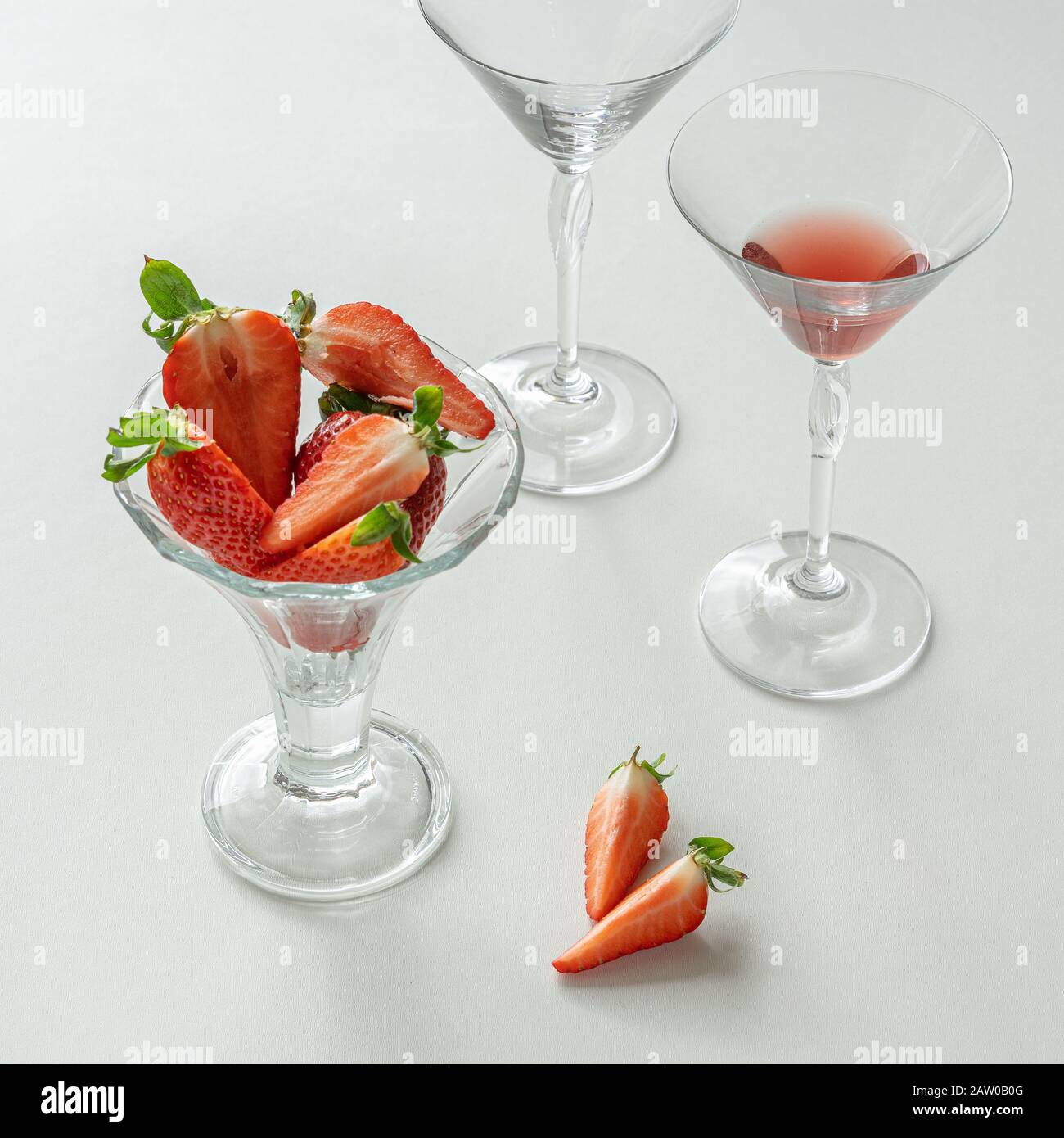 Arrangement avec fraises tranchées sur fond blanc. Des morceaux de baies sont dans le verre et sur la table. Le verre contient une boisson rouge. Une vie de premier plan Banque D'Images