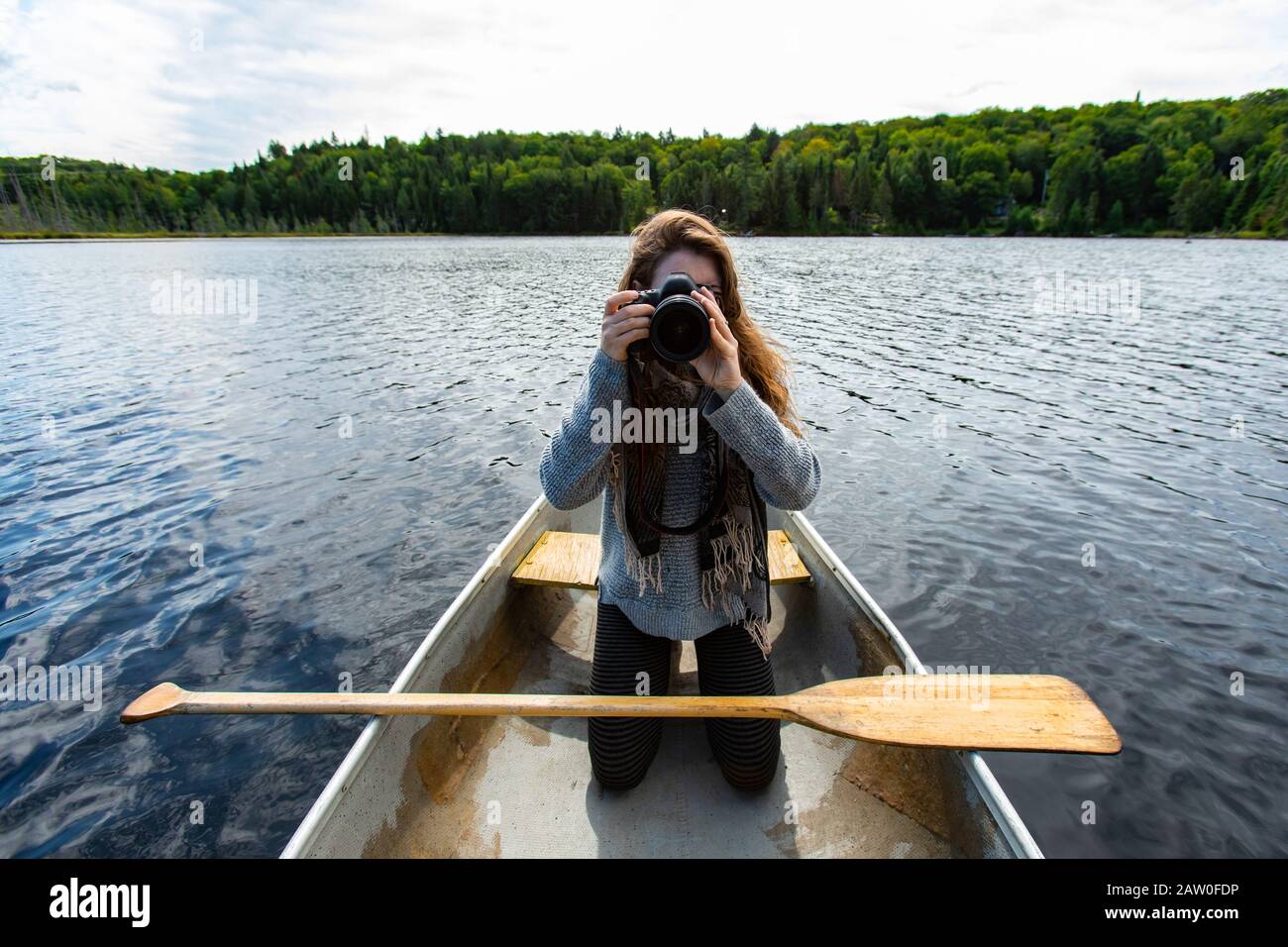 La jeune photographe féminine qui s'agenouille sur le genou clique en canoë sur des photos avec un appareil photo reflex numérique alors qu'elle est sur le lac dans le nord du Québec au Canada Banque D'Images