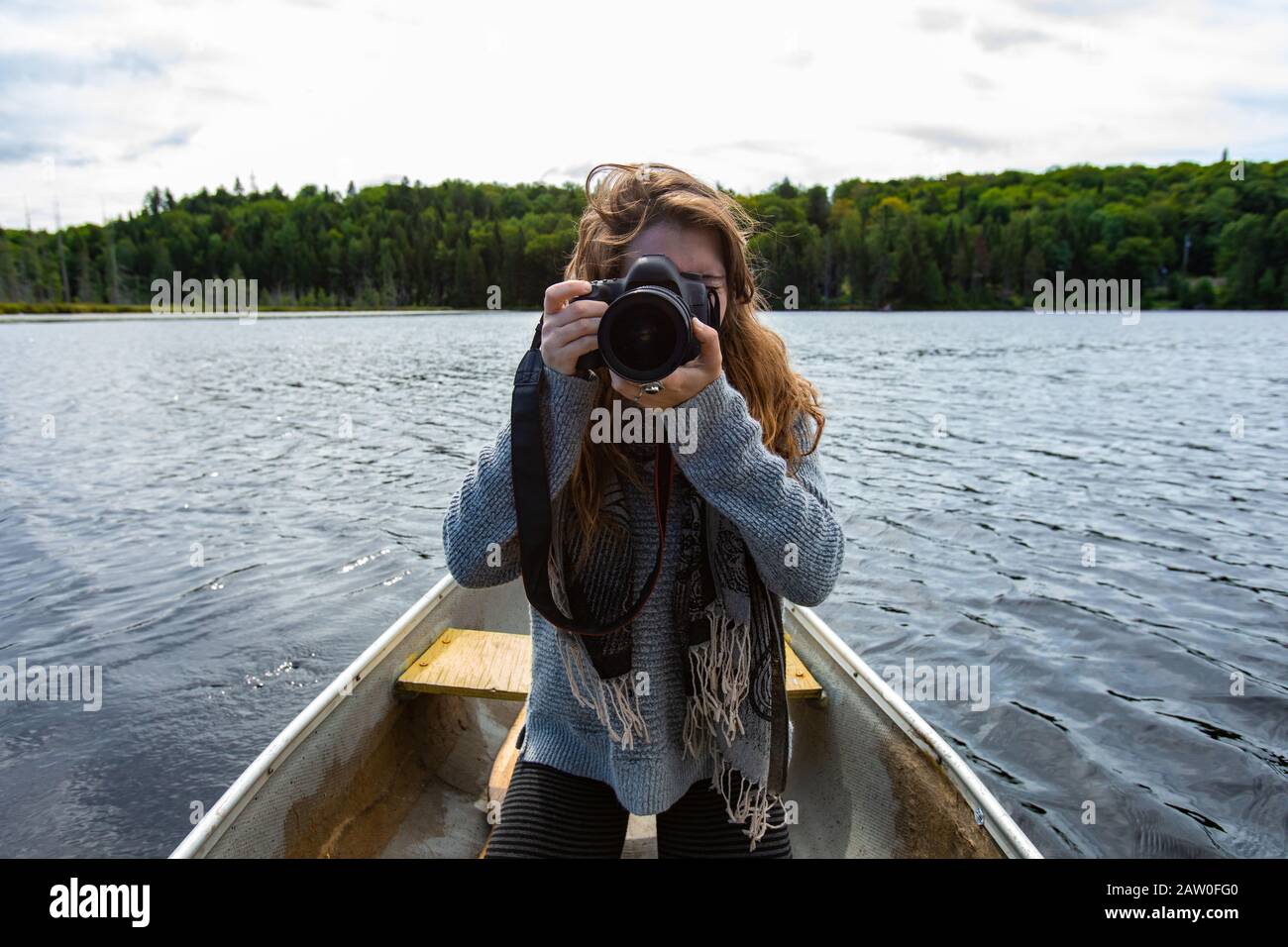 Jeune femme tenant un appareil photo reflex numérique et un objectif de réglage pour la prise de vue en canoë sur le lac dans le nord du Québec au Canada Banque D'Images